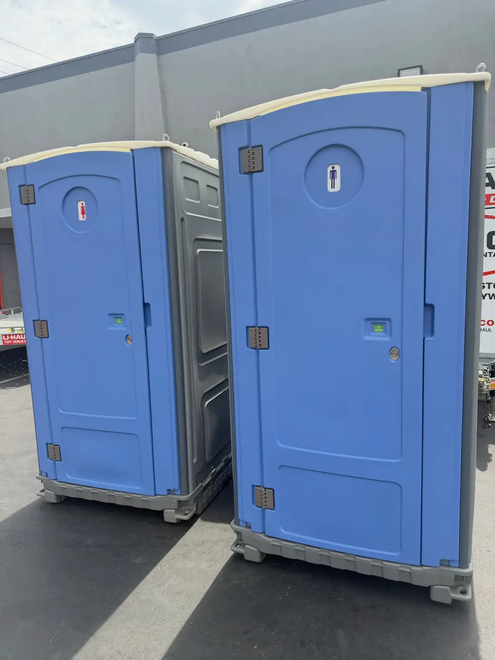 Two blue standard porta potties placed on pavement after delivery