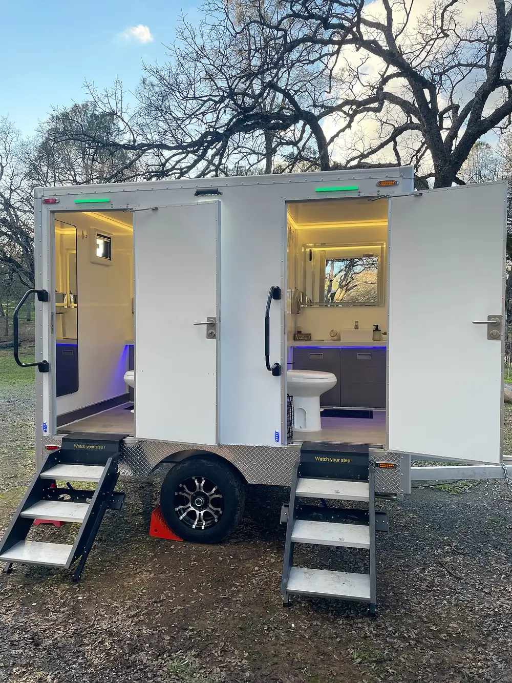 Lit two-stall restroom trailer set up for an evening event