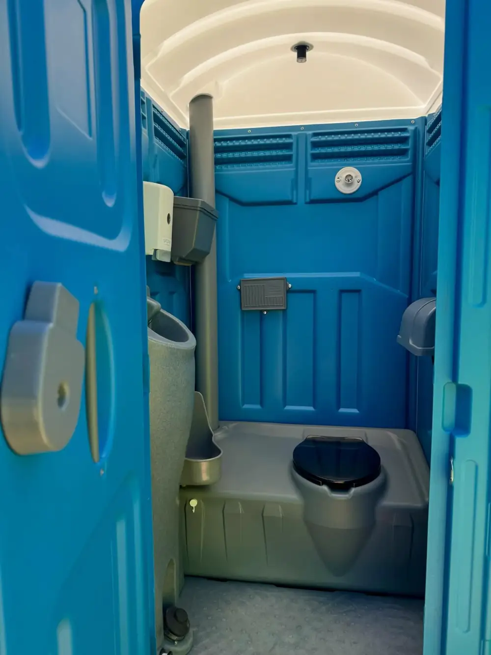 Inside a standard porta potty with a toilet seat, urinal and toilet paper holder
